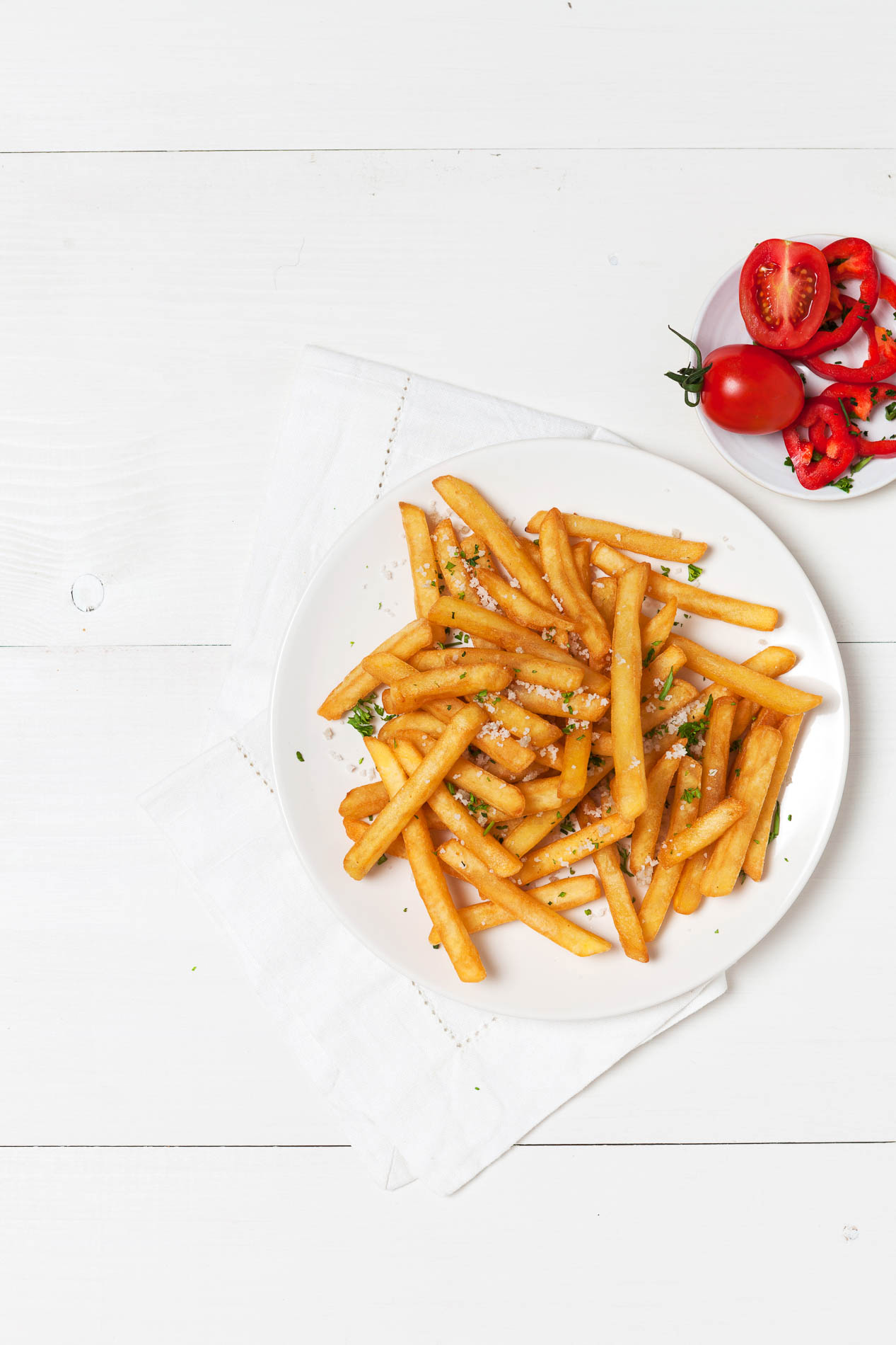 white plate with fries on a white wooden table with tomatoes