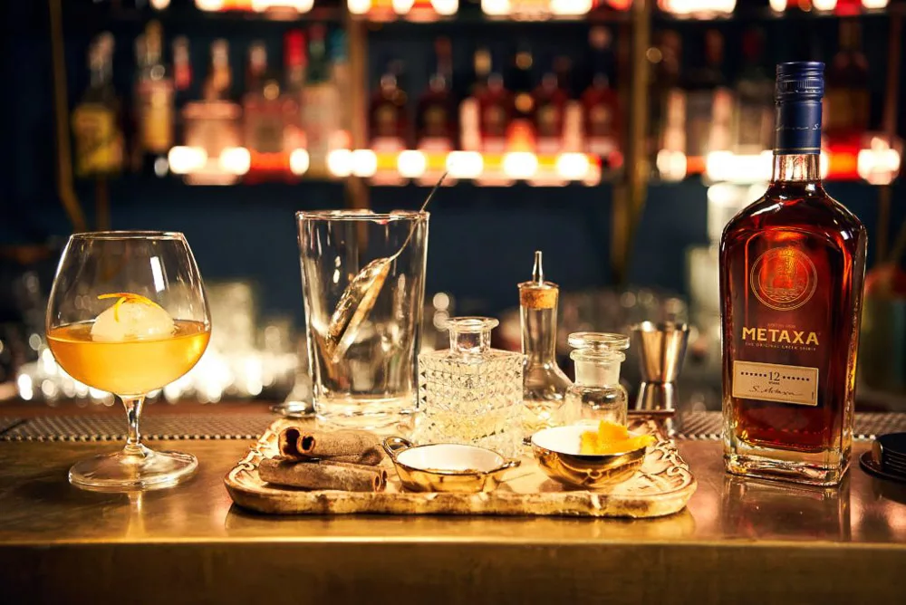beverage cocktail with ball of ice and mixologist tools and bottle of metaxa