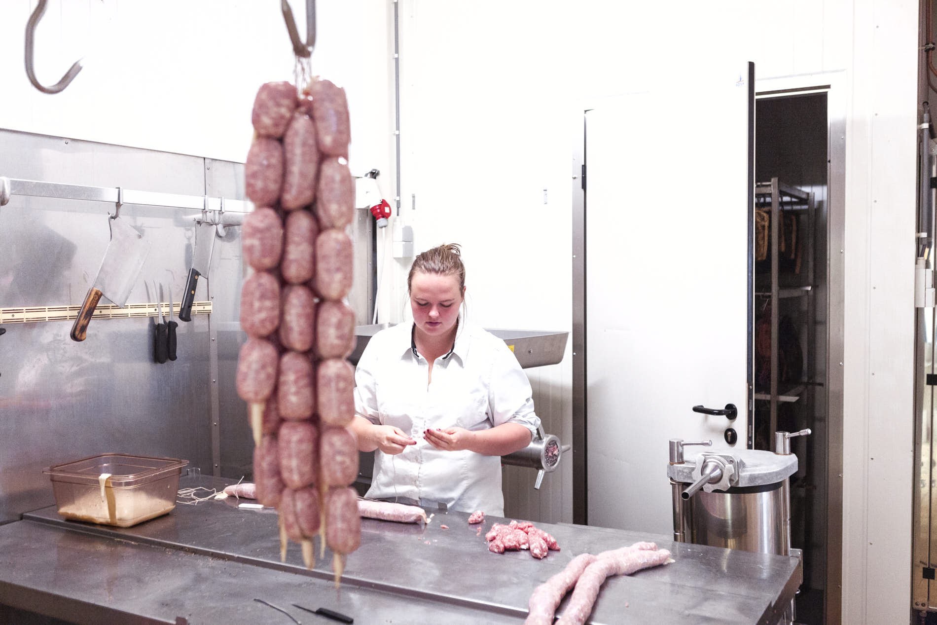 female butcher in a butchery witch fresh sausages hanging from a hook