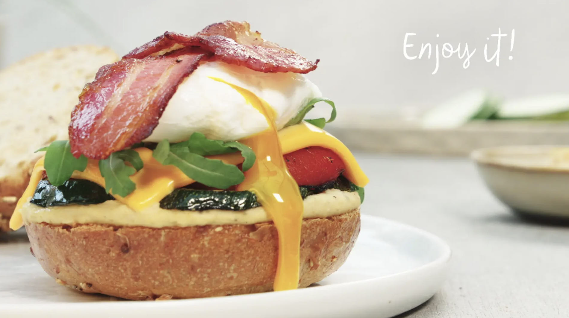 still from recipe video of a sandwich with grilled vegetables bacon and poached egg