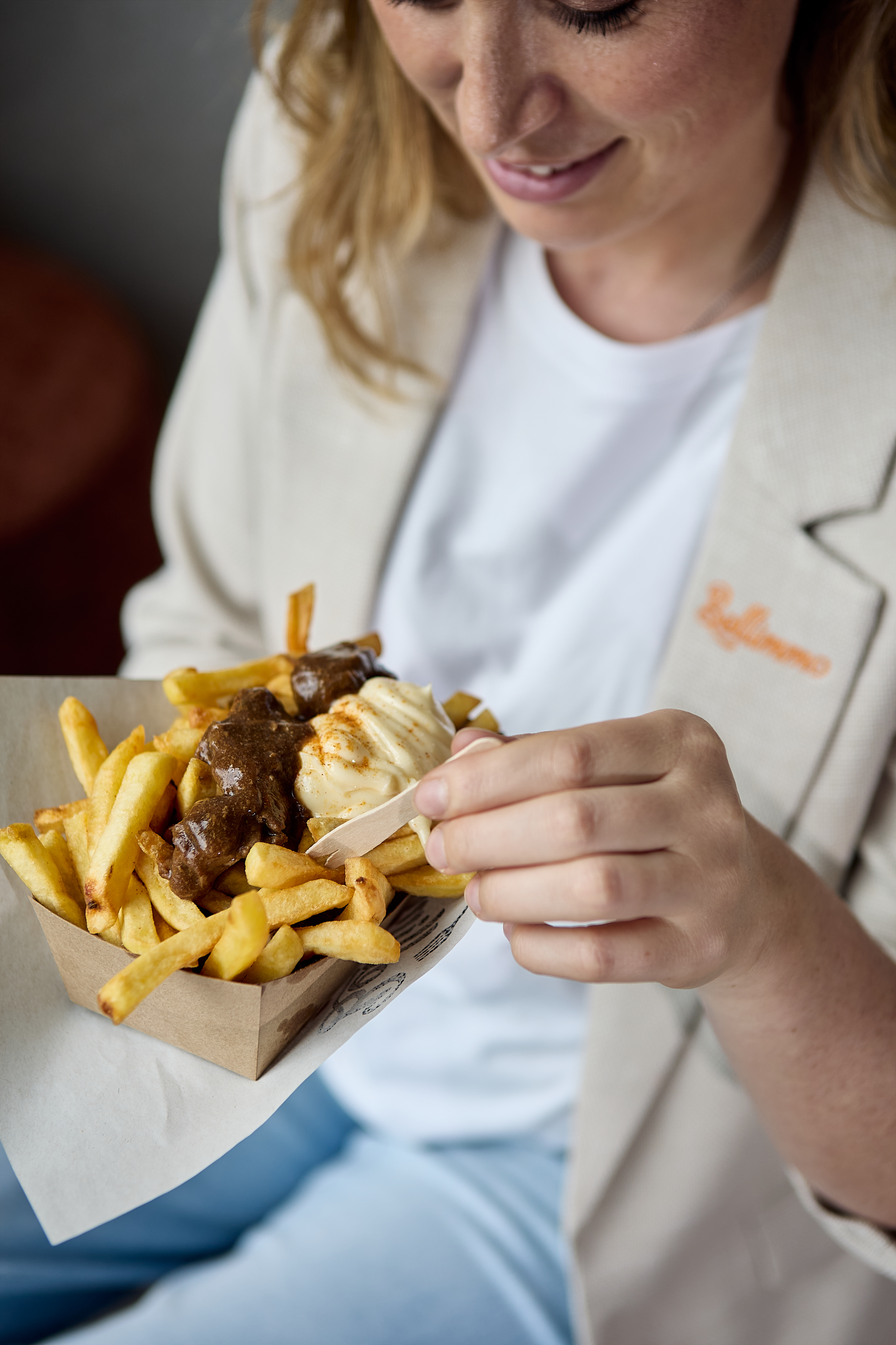 Commercial lifestyle culinary photography for Bellimmo featuring a woman enjoying classic Belgian fries served in eco-friendly paper packaging with rich beef stew and mayonnaise toppings.